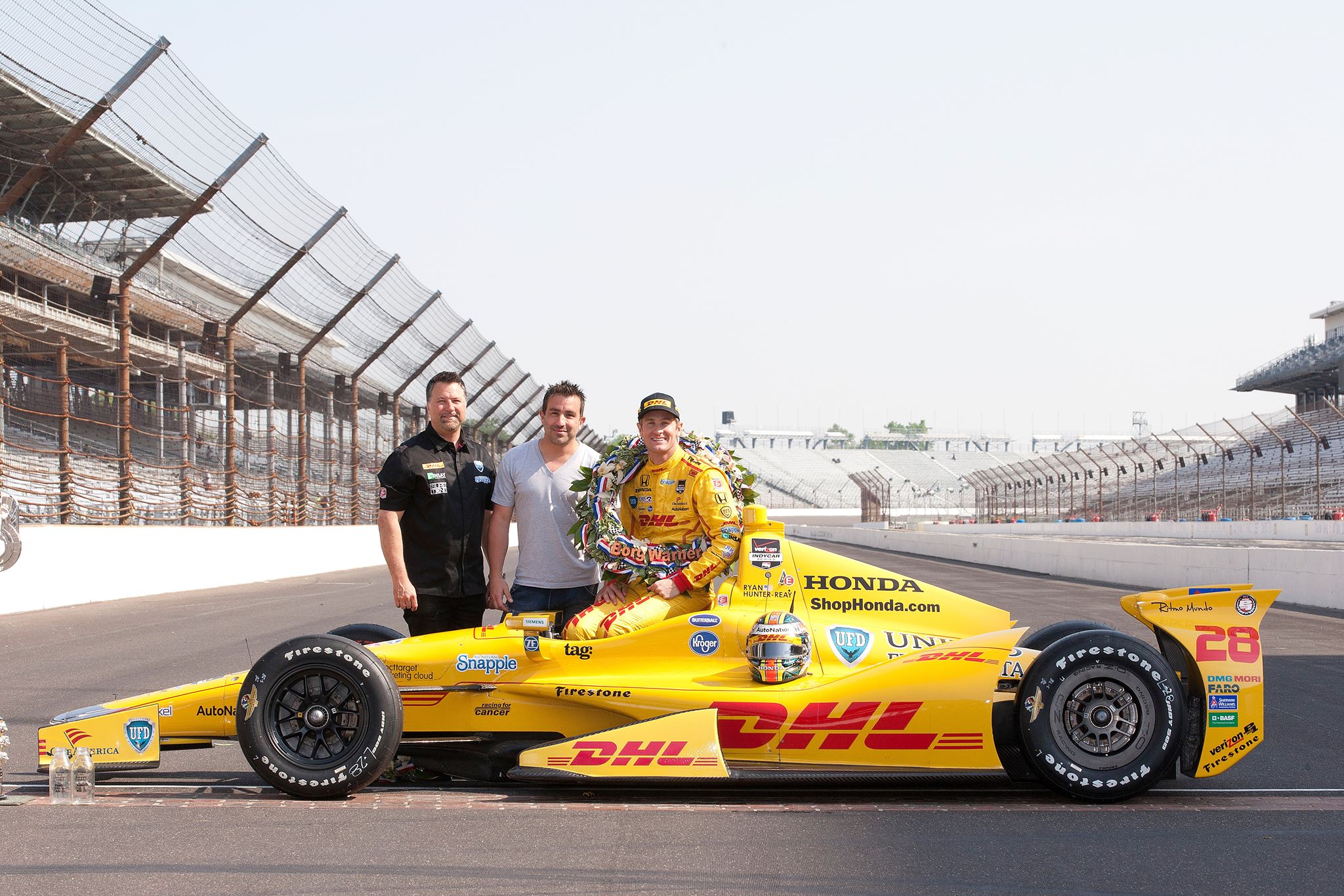 Three people standing behind an Indy 500 winning race car